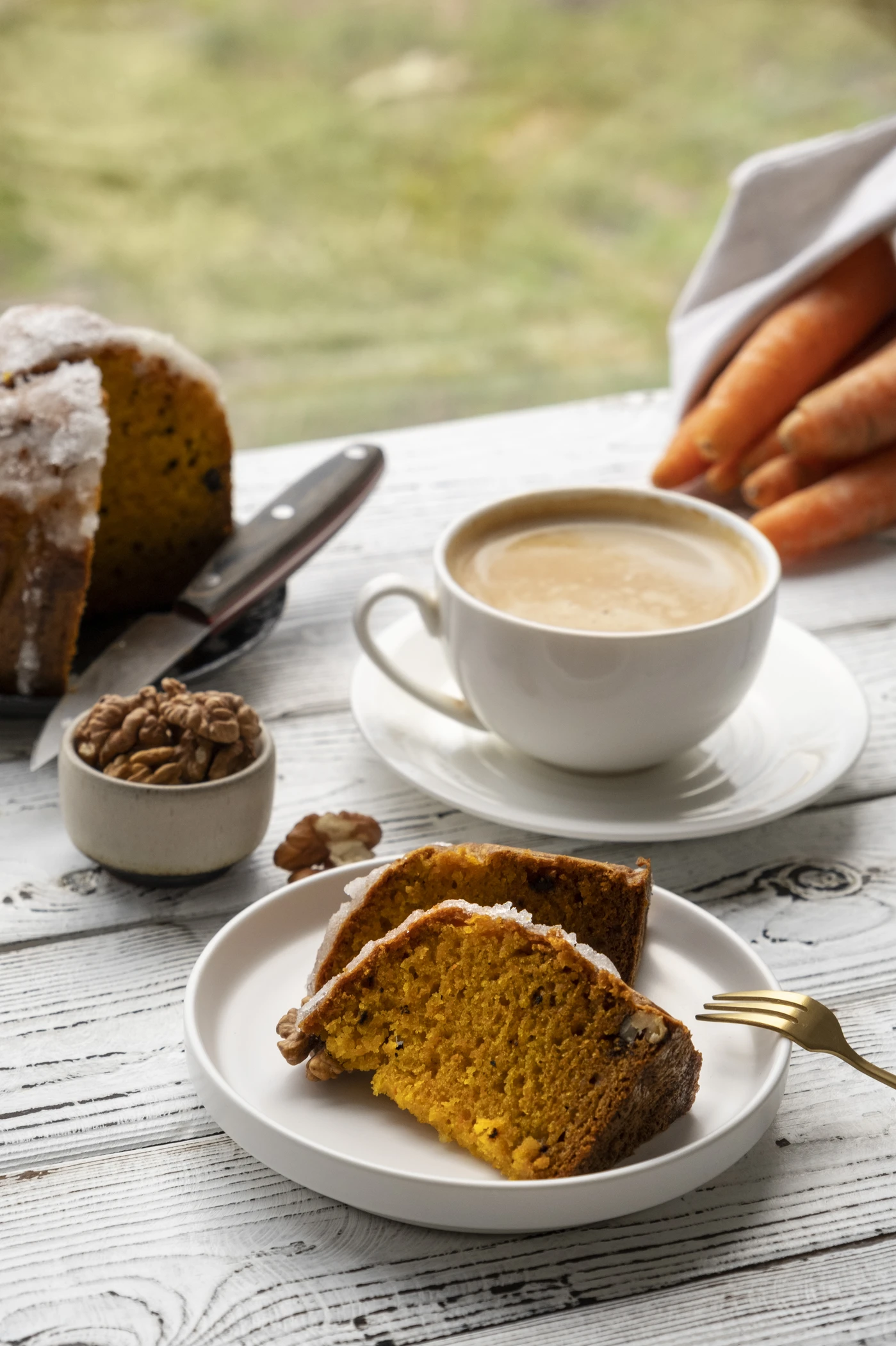 Fetta di torta alle carote servita con caff&egrave; su un tavolo di legno.